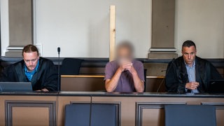 Ein wegen zweifachen Mordes und versuchten Mordes angeklagter Mann sitzt in einem Gerichtssaal des Landgerichts Verden zwischen seinen Pflichtverteidigern.