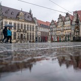 Der Marktplatz spiegelt sich in einer Regenpfütze. 