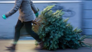 Eine Frau schleift einen Weihnachtsbaum auf die Straße.