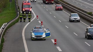 Ein Streifenwagen der Polizei steht mit Blaulicht auf einer abgesperrten Autobahnausfahrt. Im Hintergrund sind Einsatzkräfte der Feuerwehr auf der Standspur der Autobahn zu sehen.