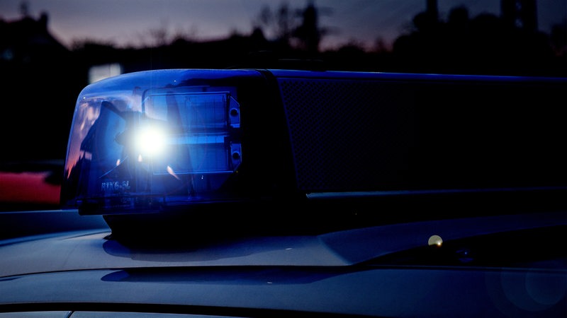 Das Blaulicht eines Polizeiwagens blinkt. Im Hintergrund dunkler Himmel und schemenhaft ein Haus.