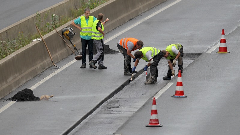 Vier Bauarbeiter reparieren eine Fahrbahn