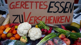 Ein Schild mit der Aufschrift „Gerettetes Essen zu verschenken“ und zahlreiche Lebensmittel liegen auf einem Tisch am Stand der Klimaaktivisten von der Initiative "Aufstand der letzten Generation".