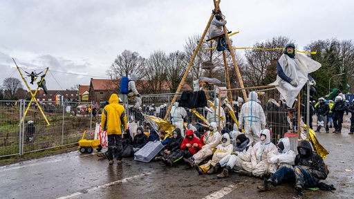 Klima-Aktivisten blockieren eine Straße. Im Hintergrund sind Polizisten zu sehen.