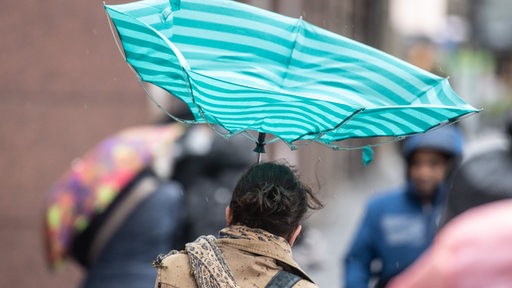 Eine Sturmböe erfasst den Regenschirm einer Frau. 