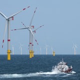 Ein Boot fährt vor Windkraftanlagen im Meer.