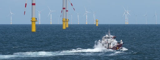 Ein Boot fährt vor Windkraftanlagen im Meer.