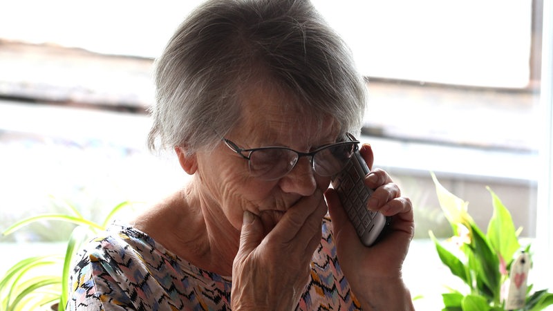 Eine ältere Frau reagiert bestürzt auf einen Anruf.