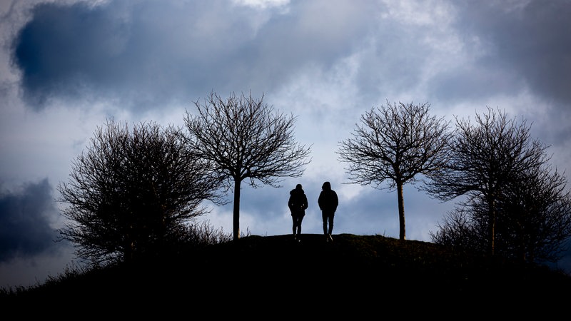 Spaziergänger gehen auf einen Hügel am Kronsberg, während bei stürmischem Wetter dunkle Wolken am Horizont vorüberziehen. Ausläufer eines Sturmtiefs sorgen am Sonntag in Niedersachsen und Bremen für starken Wind. 