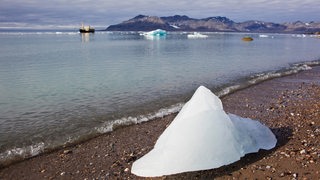 Eis am Strand von Svalbard, Spitzbergen. Im Hintergrund ein Schiff.