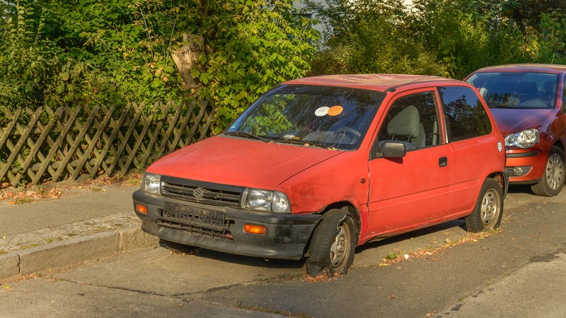 Ein roter Kleinwagen im Schrottzustand am Straßenrand.