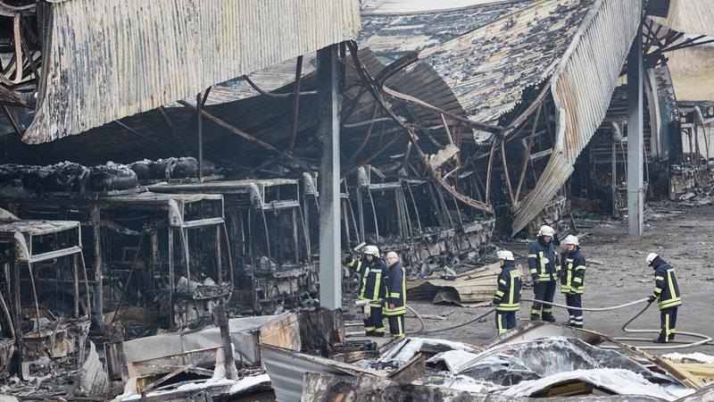 Feuerwehrmänner stehen auf dem von einem Brand zerstörten Gelände der Firma alga Nutzfahrzeug- und Baumaschinen GmbH. Bei einem Großbrand in Sittensen im Landkreis Rotenburg ist in der Nacht zu Sonntag ein erheblicher Sachschaden entstanden. 