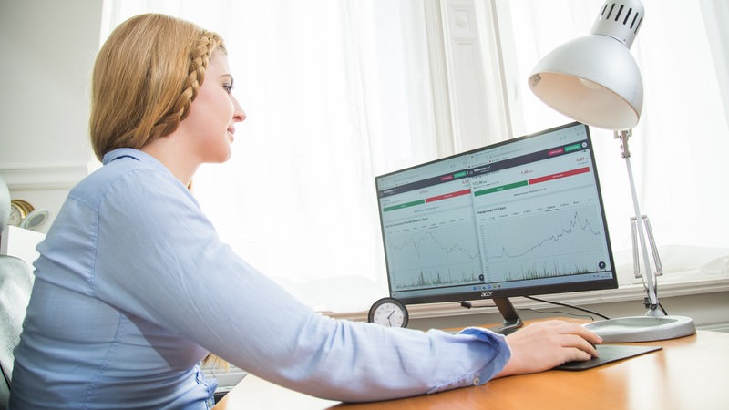 Eine Frau sitzt vor einem PC mit verschiedenen Aktien-Charts (Symbolbild).