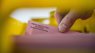 Eine Hand zieht einen Briefumschlag zur Sozialwahl aus einer Kiste