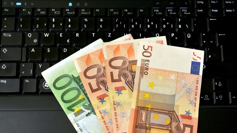 Auf einem Laptop liegen mehrere Euro-Scheine.
