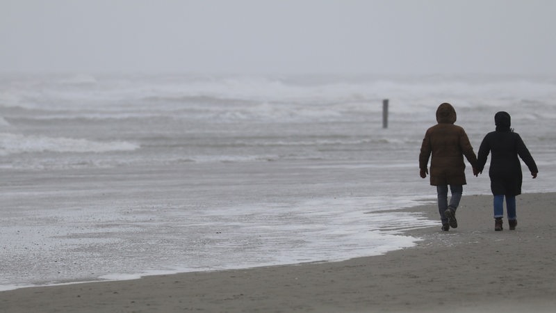 Spaziergänger gehen bei stürmischem Wetter am Strand der ostfriesischen Insel Norderney