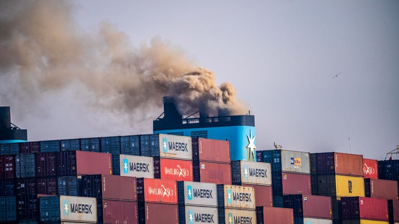 Aus dem Schornstein eines Containerschiffes kommt dicker dunkler Rauch.