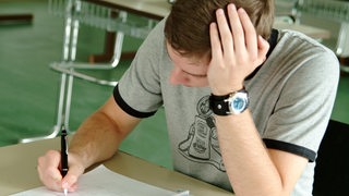 Ein Oberstufenschüler stützt seinen Kopf auf und schreibt etwas in sein Heft