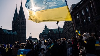 Die ukrainische Nationalfahne weht während der Kundgebung gegen den Krieg in der Ukraine auf dem Domshof im Wind. 