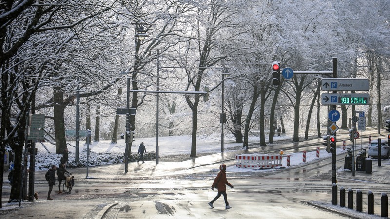 Passanten gehen unter mit Schnee bedeckten Bäumen am Wall. Bei Temperaturen um den Gefrierpunkt zeigt sich die Hansestadt noch einmal winterlich.