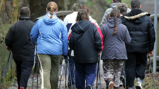 Rückansicht einer Gruppe leicht übergewichtiger Menschen beim Nordic Walken.