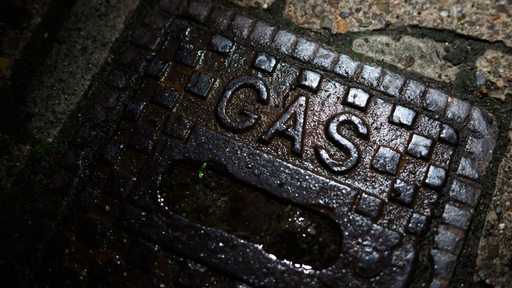 Ein Schriftzug „Gas“ steht in einem Wohngebiet auf einer gusseisernen Straßenkappe einer Gasleitung.