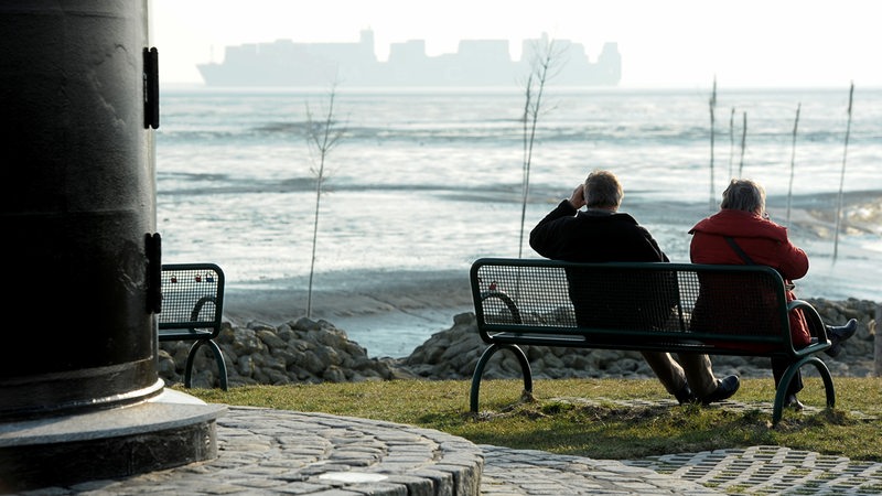 Zwei Senioren sitzen auf einer Bank an Bremerhavens Küste