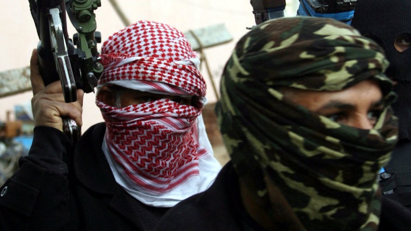 Symbolbild zeigt zwei vermummte IS Terroristen, einer hält seine Waffe nach oben.
