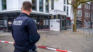 Ein Polizist steht in der Nähe des Tatorts einer gewaltätigen Auseinandersetzung in Bremen an einem Absperrband. 