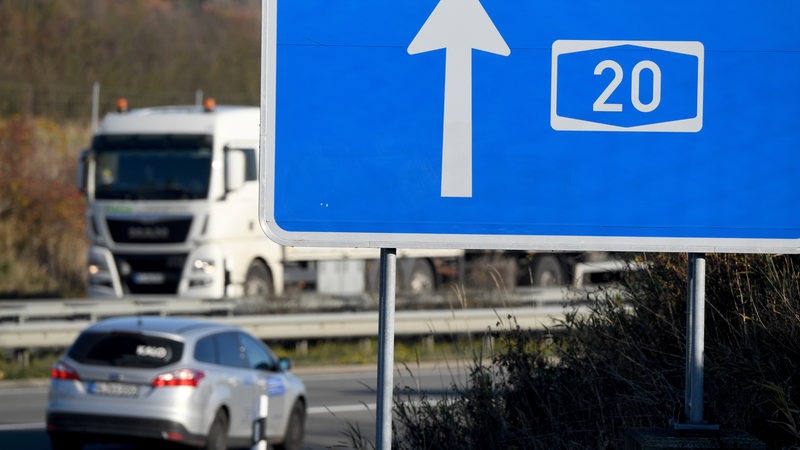 Autos fahren hinter einem Hinweisschild zur A20 auf der Autobahn. 