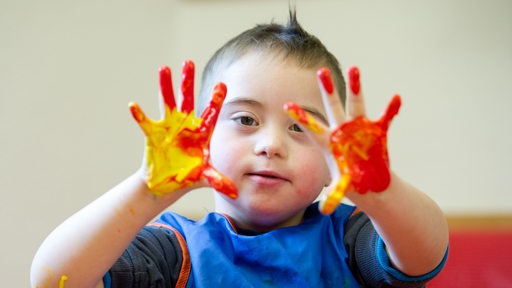 Junge mit Down-Syndrom spielt mit Fingermalfarben