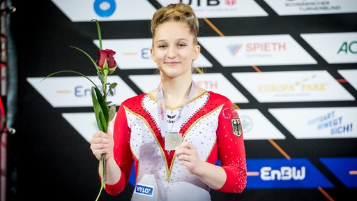 Karina Schönmaier zeigt stolz ihre Silber-Medaille und hält dabei eine Rose.