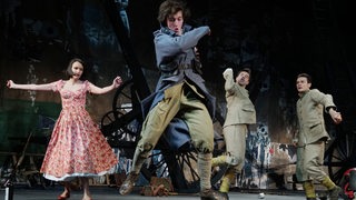 Drei Männer und eine Frau tanzen auf einer Bühne.