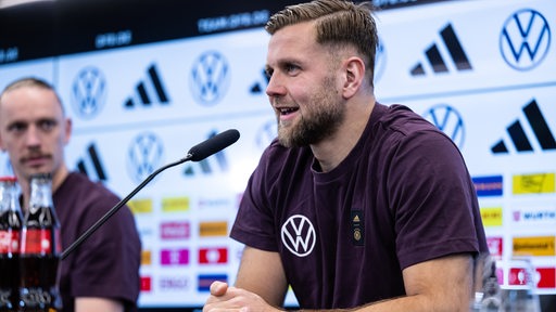Werder-Stürmer Niclas Füllkrug sitzt lächelnd bei einer Pressekonferenz der deutschen Nationalmannschaft.