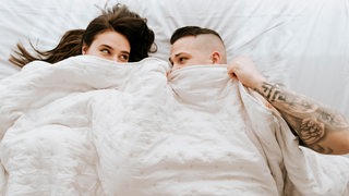 Ein Paar liegt unter einer Decke und schaut sich in die Augen