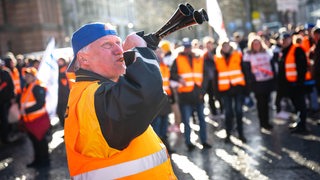 Ein Demonstrant steht mit einem Signalhorn vor Demonstranten am Bremer Hauptbahnhof. 
