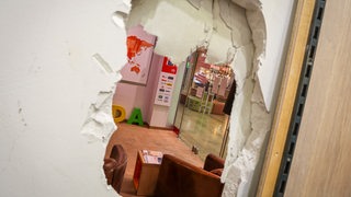 Durch ein Loch in einer Wand kann man in ein Geschäft sehen.