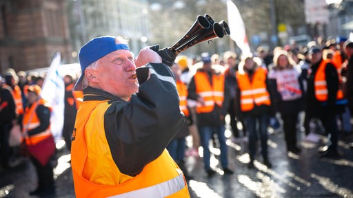 Ein Demonstrant steht mit einem Signalhorn vor Demonstranten der Eisenbahn- und Verkehrsgewerkschaft (EVG) mit Plakaten am Hauptbahnhof