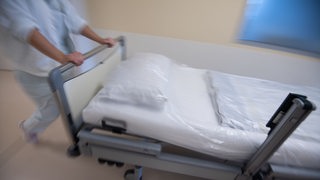 Eine Krankenpflegerin schiebt ein Krankenbett durch einen Gang einer Station