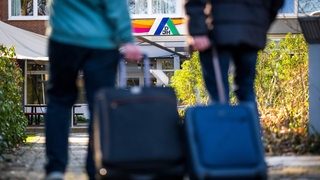 Gäste stehen mit Koffern und Taschen vor einer Jugendherberge.