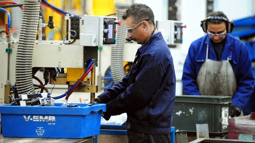 Arbeiter in Arbeitsanzügen stehen mit Schutzbrille an Geräten
