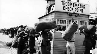 Soldaten mit Seesäcken stehen in einer Schlange an einer Bude.