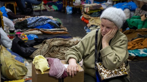 Eine trauernde ältere Ukrainerin sitzt mit vielen anderen Menschen zum Schutz vor der russischen Bombardierung in einer U-Bahn Station in Charkiv