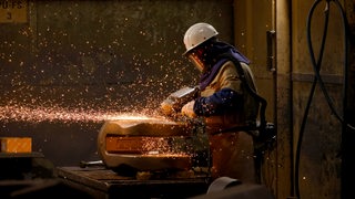 Ein Arbeiter flext ein fertiges Stahlbauteil 