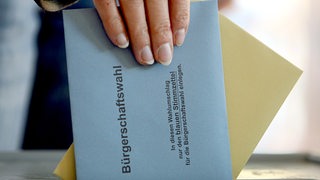 Eine Hand steckt zwei Umschläge in eine Wahlurne