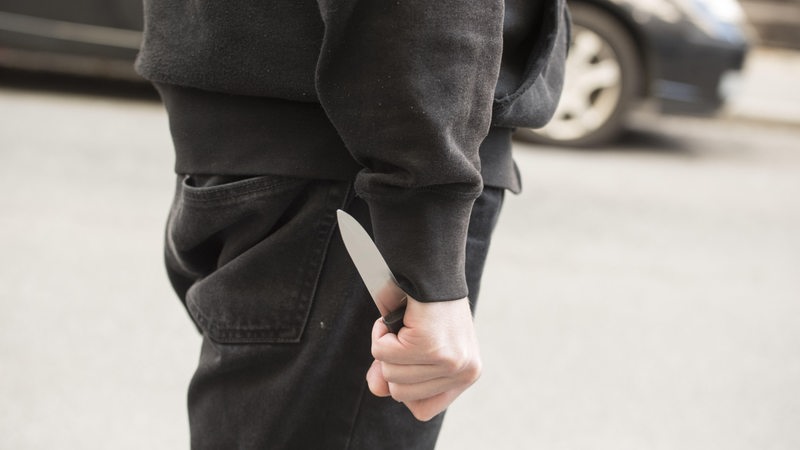 Ein Mann mit einem Messer in der Hand steht vor einem Auto.