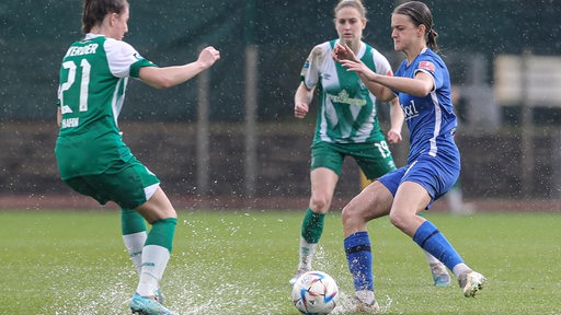 Die Werder-Spielerin Chiara Hahn im Zweikampf mit Meppens Anna Margraf bei aufspritzendem Regenwasser auf dem Rasen.