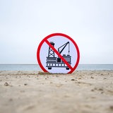 Ein Plakat gegen die geplante Erdgasförderung steckt im Sand des Strandes von Borkum.