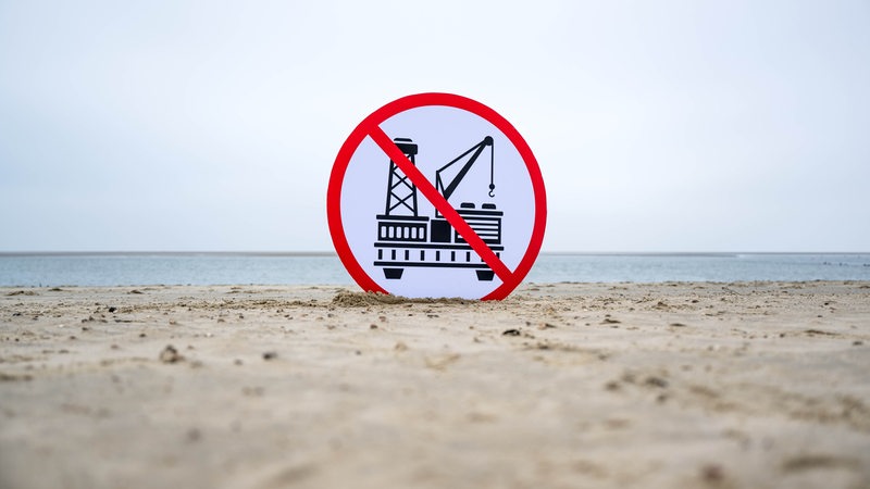 Ein Plakat gegen die geplante Erdgasförderung steckt im Sand des Strandes von Borkum.