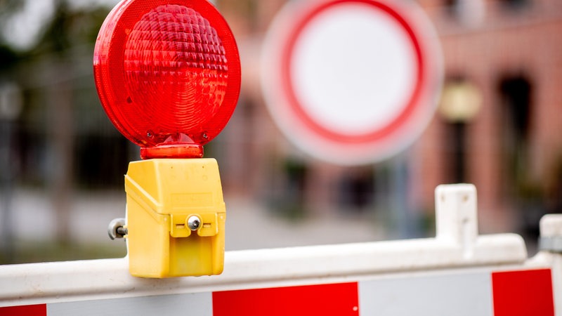 Eine rote Warnleuchte hängt an einer Baustelle vor einem Verkehrsschild, das auf die verbotene Durchfahrt für Fahrzeuge aller Art hinweist.
